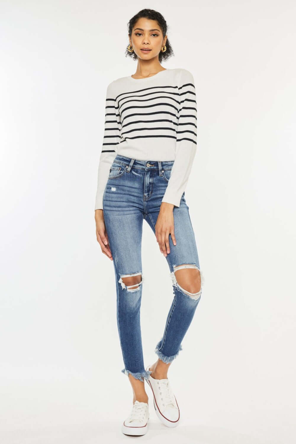 Model wearing high waist distressed raw hem ankle skinny jeans with striped long-sleeve top and white sneakers, trendy and edgy fashion look