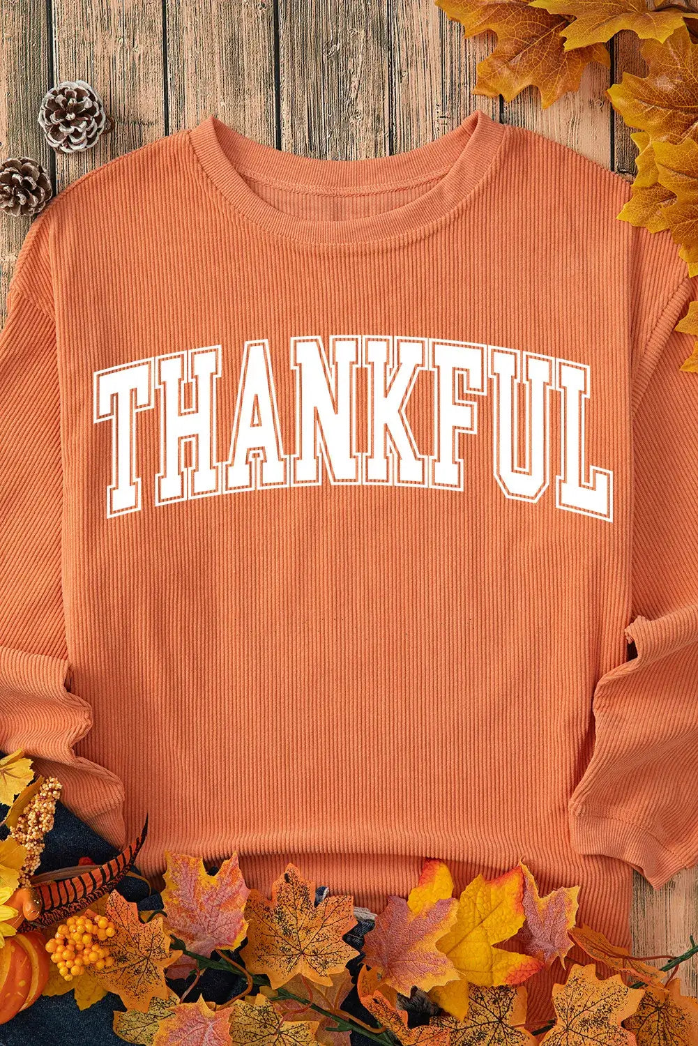 Bella Road THANKFUL round neck long sleeve sweatshirt, orange color, autumn-themed background with leaves, pinecones, and pumpkins.