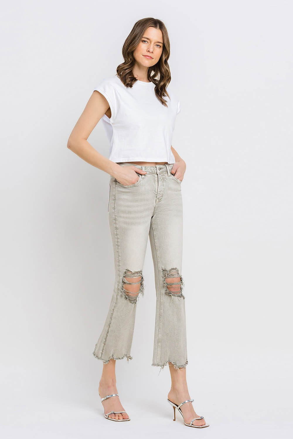 Woman wearing Lovervet Distressed Raw Hem Cropped Flare Jeans with a white top and high heels.