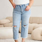 Woman wearing Tummy Control High Waist Raw Hem Distressed Jeans by RFM Jeans standing in a stylish living room.