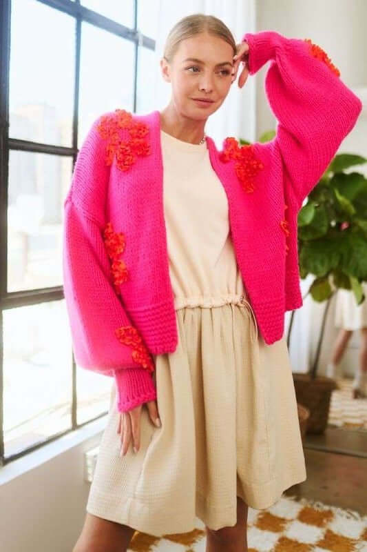 Model showcasing a vibrant pink floral applique cardigan over a casual cream dress, perfect for layered looks.