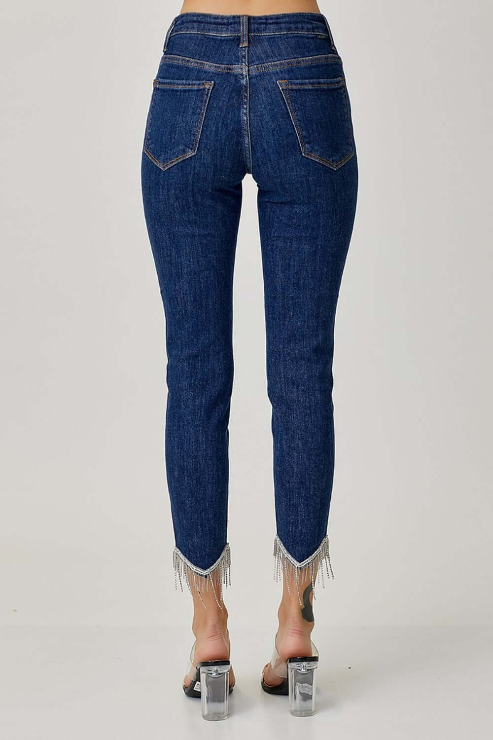 Back view of RISEN Full Size Embellished Mid Rise Crop Skinny Jeans with fringe hem and mid-rise fit showing two back pockets.