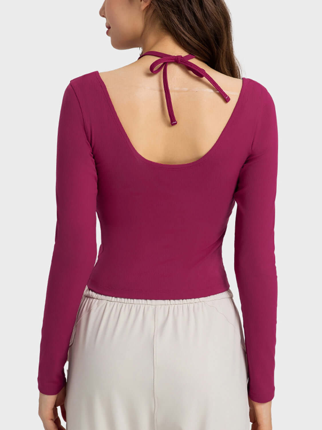 Back view of a woman wearing a fuchsia Millennia halter neck sporty top with long sleeves, showcasing its stylish design.