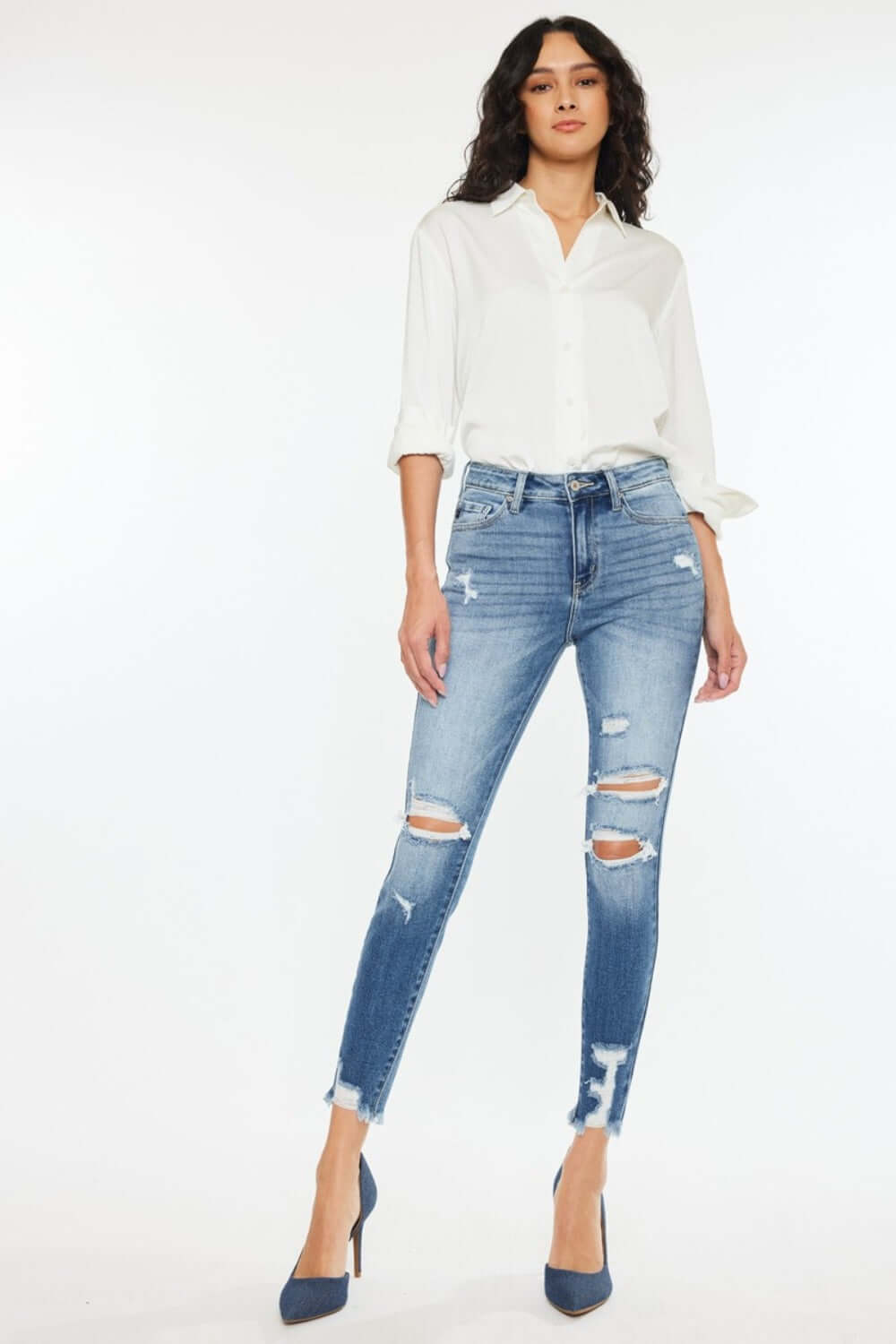 Woman wearing High Rise Frayed Ankle Skinny Jeans in medium wash with distressed detailing and fray hem, paired with a white button-up shirt.