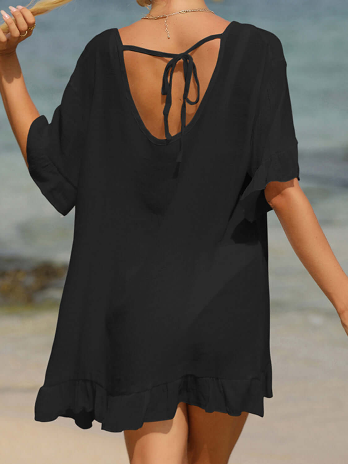 Woman wearing black tied ruffled half sleeve cover-up on beach, back view