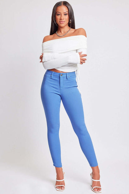 Woman wearing YMI Jeans Hyperstretch Mid-Rise Skinny Pants in vibrant blue, paired with a chic white off-shoulder top and white heels.