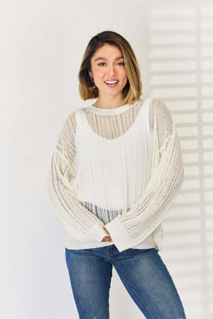 Woman wearing an Openwork Ribbed Trim Long Sleeve Knit Top in white paired with blue jeans, showcasing the stylish and modern design