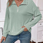 Woman wearing a striped half zip long sleeve t-shirt in light green, paired with blue jeans.