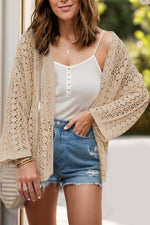 Woman wearing beige open front dropped shoulder openwork cardigan over white tank top and denim shorts.