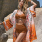 Stylish woman in orange bikini and floral cover-up enjoying the sunny beach, radiating holiday vibes.