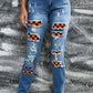 Woman wearing Bella Road distressed straight jeans with Halloween-themed patches and pockets in front of a textured background