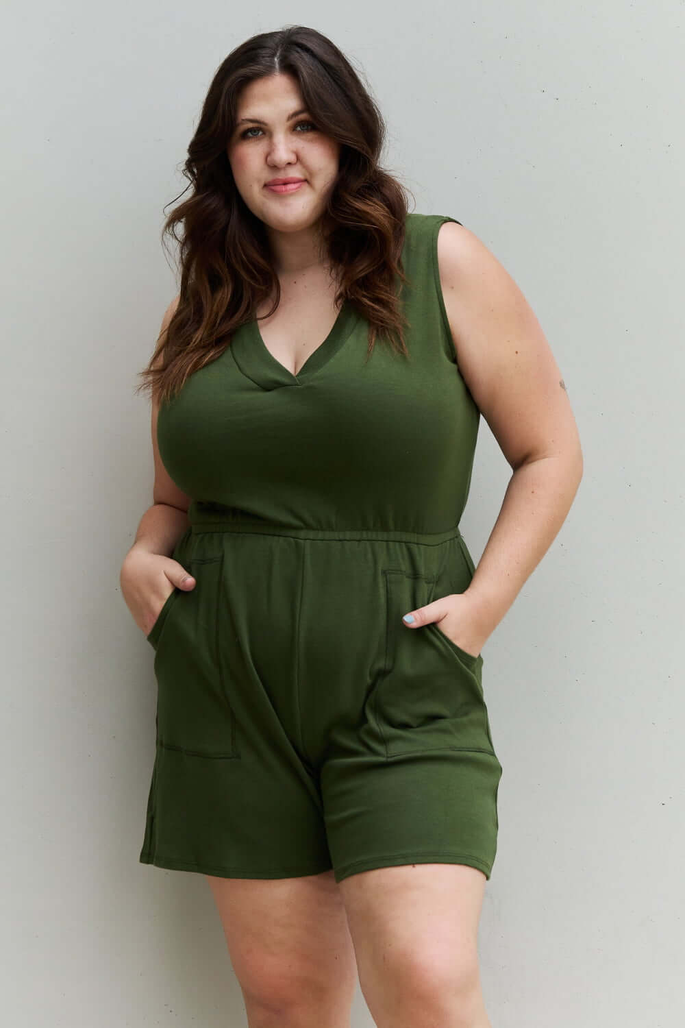 Plus-size model wearing Forever Yours V-Neck Sleeveless Romper in Army Green with pockets for casual outdoor activities.