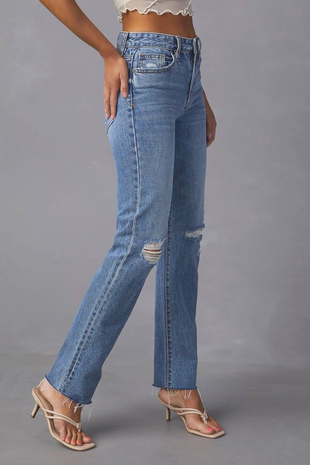 Woman wearing distressed raw hem straight jeans with pockets, featuring a trendy ripped design and moderate stretch for a chic casual look