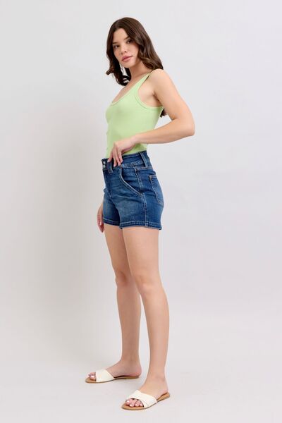 Model showcasing Judy Blue plus size double button waistband denim shorts with a green top.