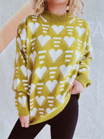 Woman wearing Bella Road Heart Contrast Long Sleeve Dropped Shoulder Sweater in yellow with white heart pattern, standing against a wall.