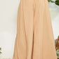 Wide leg pants with wrap pleating detail, displayed in tan color on a model, showcasing chic and flattering fit.