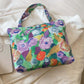 Colorful printed canvas handbag with floral design, medium size, zipper closure, resting on white fabric background