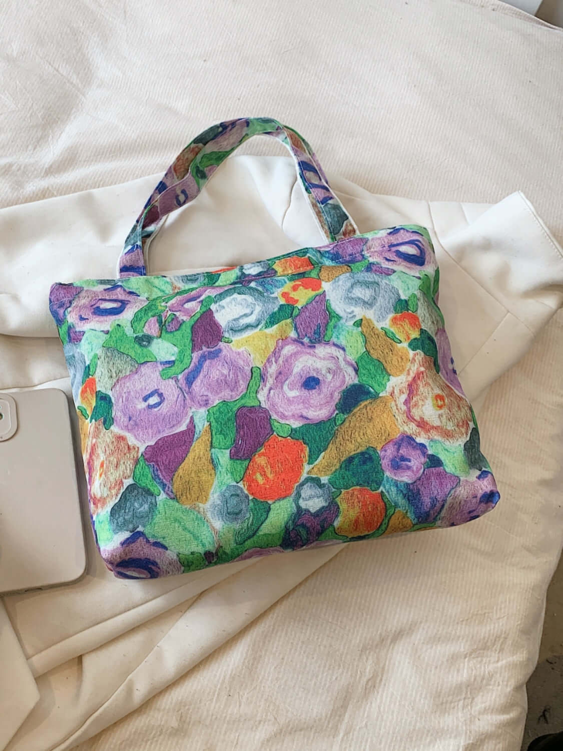 Colorful printed canvas handbag with floral design, medium size, zipper closure, resting on white fabric background