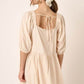 Back view of a chic beige mini dress with pintuck detail and tie-back design, showcasing playful puff sleeves.