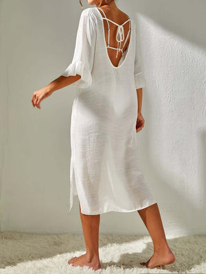 Woman wearing a white slit V-neck cover-up with flounce sleeves, backless design, and tied detail.