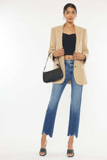 Stylish woman in Kancan high-rise slim straight jeans with frayed hem, black top, beige blazer, and black handbag, ready for a chic outing.