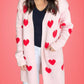 Woman wearing a Bella Road Heart Open Front Long Sleeve Cardigan with red hearts on a pink background.