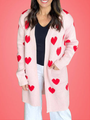 Woman wearing a Bella Road Heart Open Front Long Sleeve Cardigan with red hearts on a pink background.