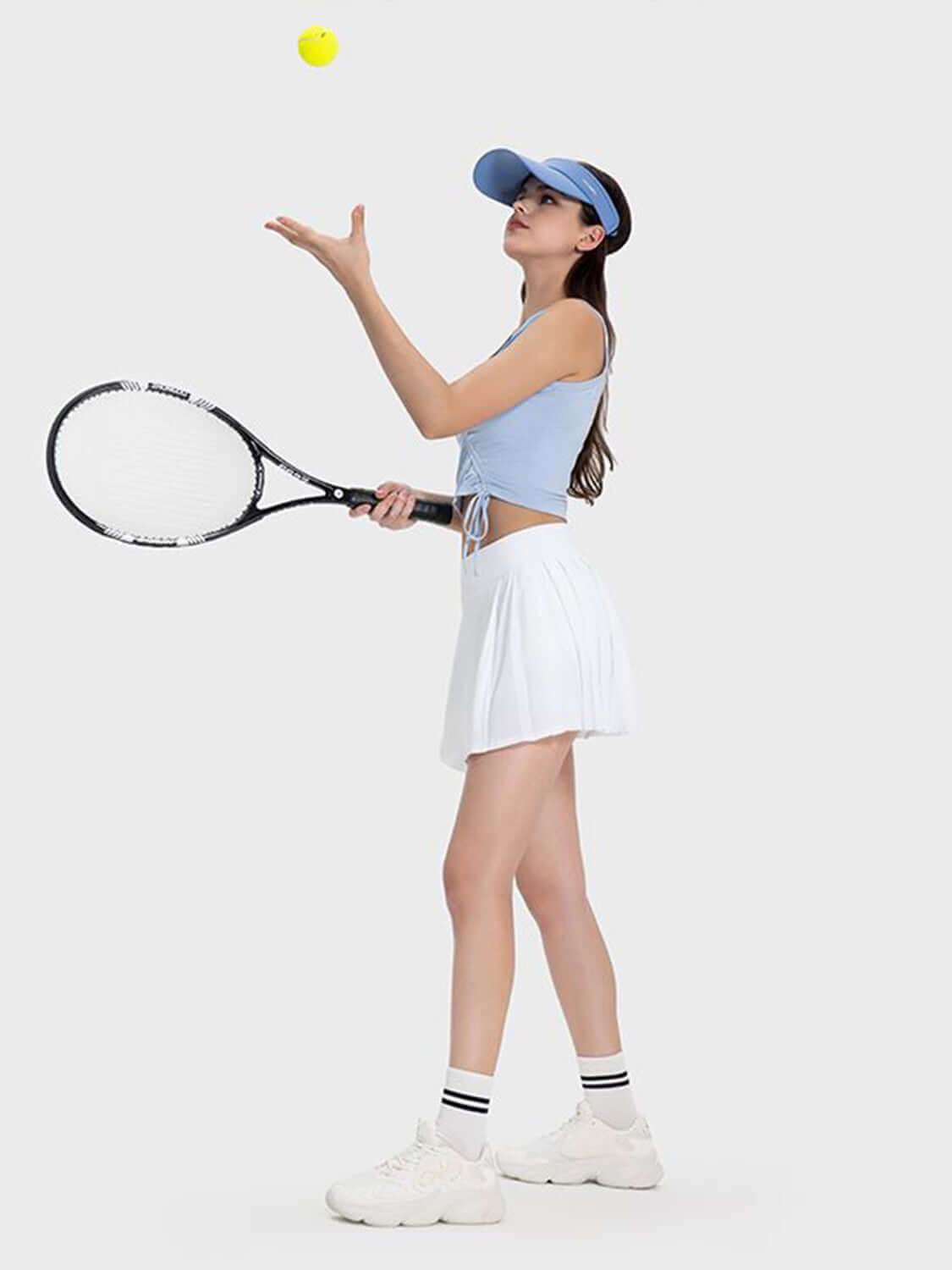 Woman in a mid-rise active skirt playing tennis, tossing a ball, showcasing sporty style and comfort.