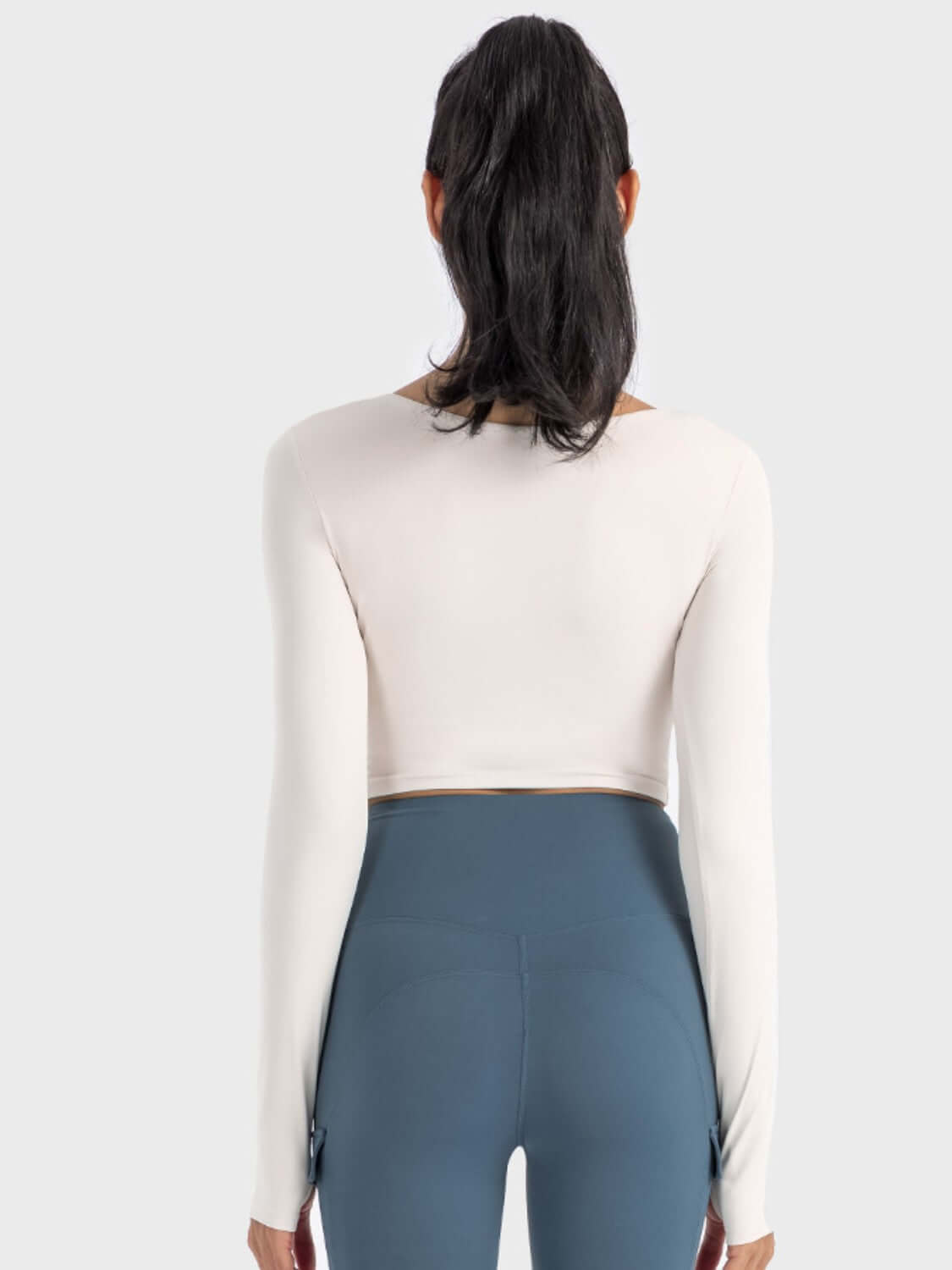 Back view of a woman wearing the Millennia Ruched Cropped Long Sleeve Sports Top with fitted leggings.