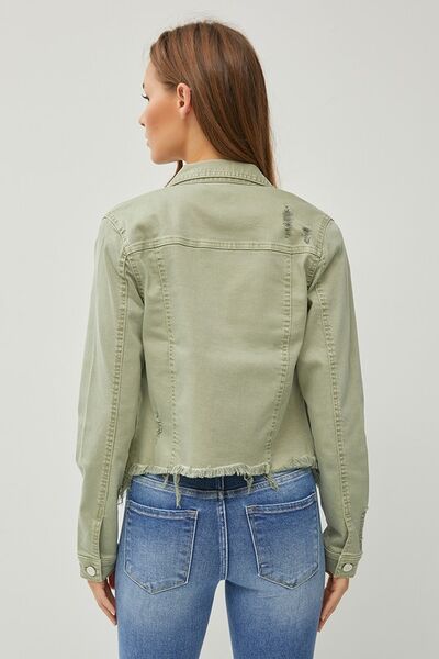 Back view of a trendy cropped denim jacket with raw hem, paired with stylish jeans, showcasing modern fashion.