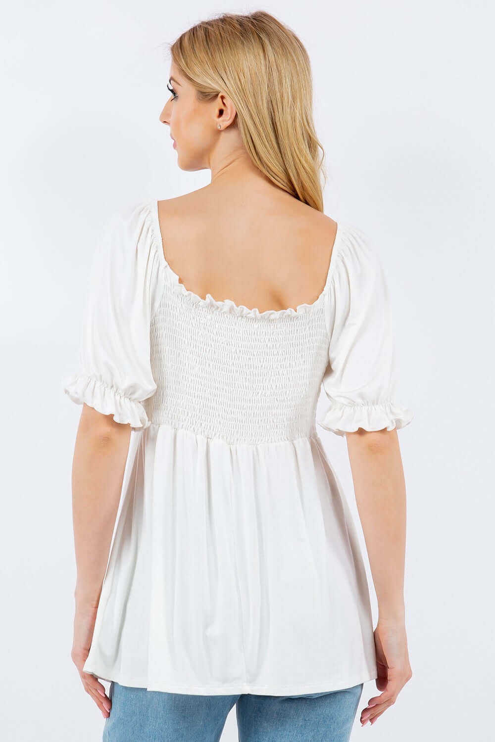 Woman wearing a white ruffled short sleeve smocked blouse with a flattering back view.