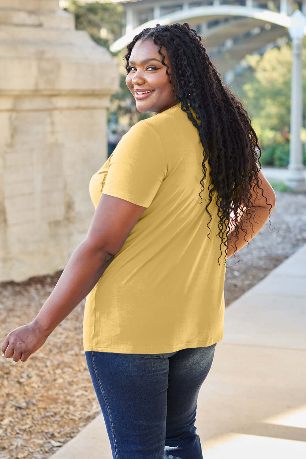 Woman wearing yellow Basic Bae Bamboo V-Neck Short Sleeve T-Shirt in outdoor setting.