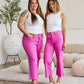 Two women wearing bright pink RFM Jeans with white tops, standing together in a stylish living room setting.