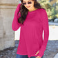 Woman wearing a round neck long sleeve fuchsia t-shirt paired with blue jeans and sunglasses outdoors.