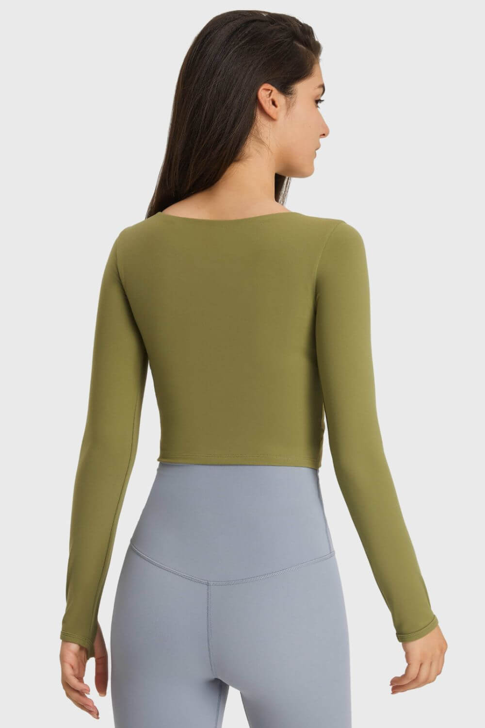 Back view of the olive green Millennia Cutout Long Sleeve Cropped Sports Top paired with light blue leggings in a studio setting.