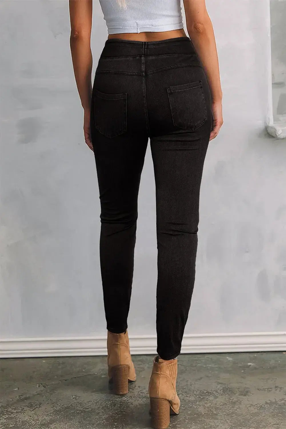 Petite woman wearing black skinny jeans with pockets, showcasing a sleek and flattering fit, standing against a simple background.