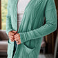 Woman wearing a textured open front cover up with pockets in green, made of 97% polyester and 3% elastane, slightly stretchy, cozy and stylish.