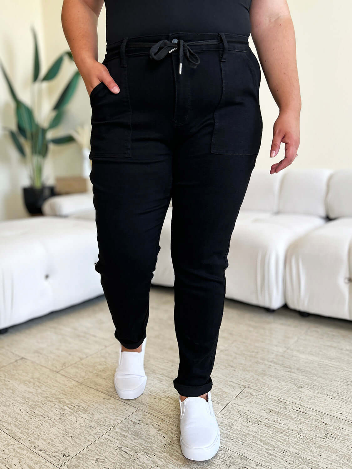 Woman wearing black high waist drawstring pants with white sneakers in a modern living room setting