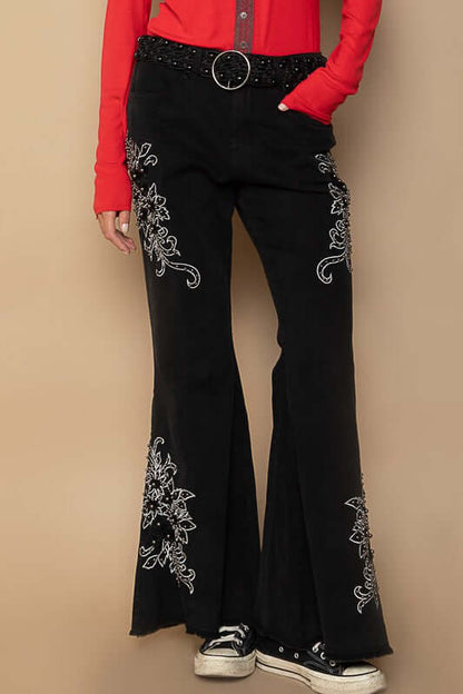 Black flare pants with raw hem and intricate embroidery, styled with a bold red top and sneakers.