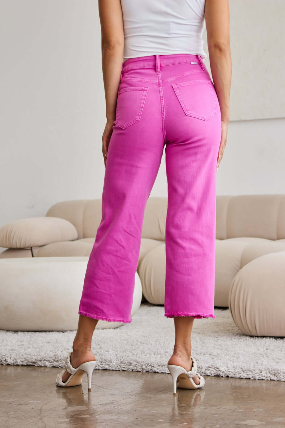 Woman wearing RFM Jeans Crop Chloe Full Size Tummy Control High Waist Raw Hem Jeans in vibrant pink, back view.