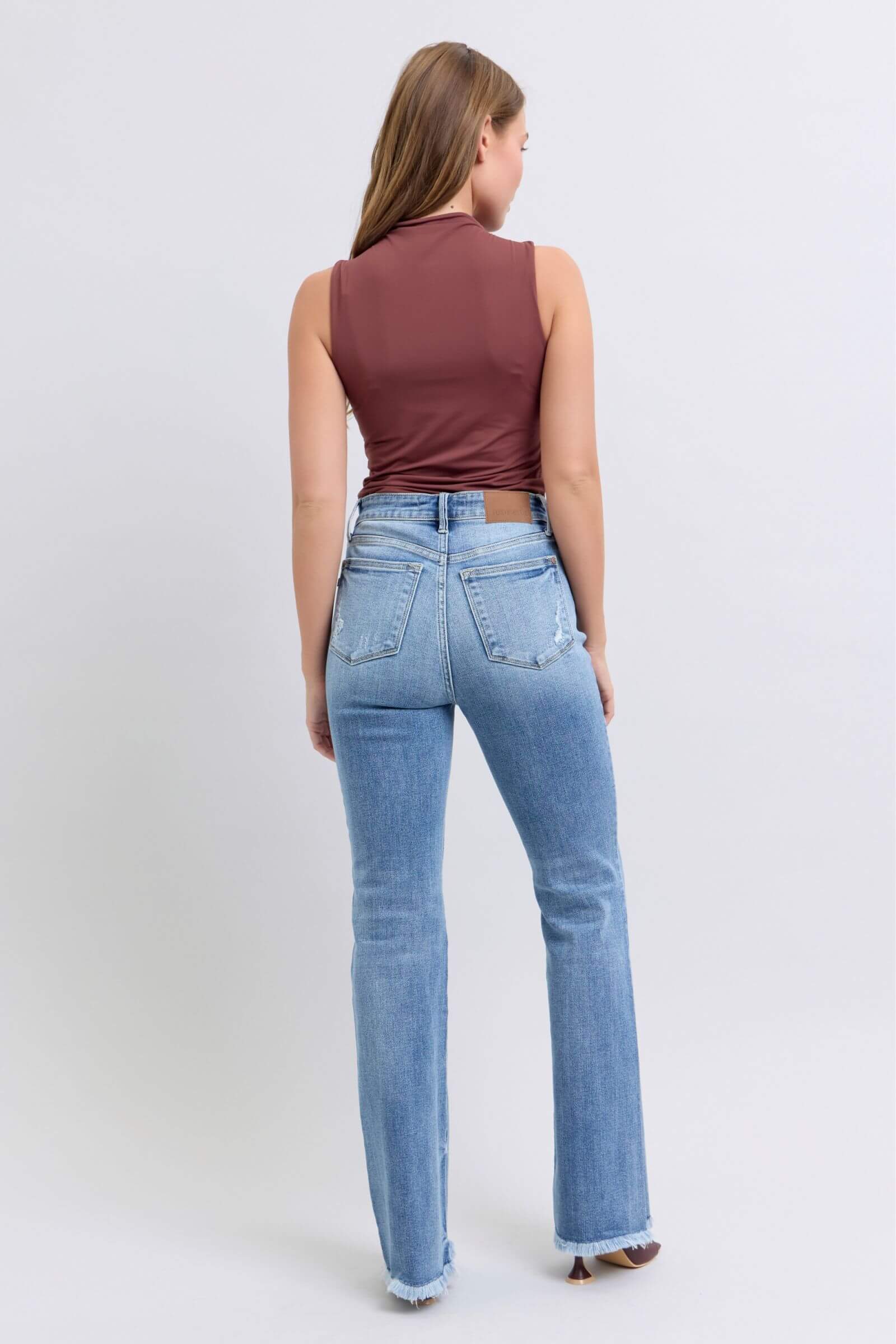 Back view of a model wearing Judy Blue high rise bootcut jeans with raw hem and a fitted top, showcasing a trendy outfit.