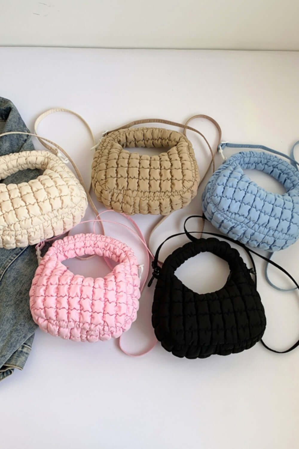 Quilted puffy crossbody bags in beige, blue, pink, and black with removable straps, displayed on a surface for fashion versatility.