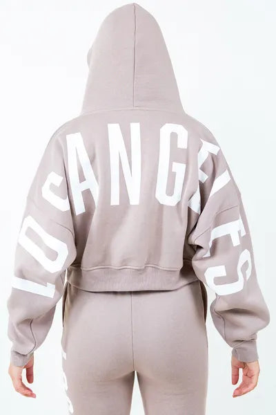 Back view of American Bazi 'Los Angeles' cropped hoodie in beige, featuring bold white lettering and a drawstring hood.