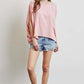 Woman wearing pink oversized boat neck top with denim shorts and sandals, showcasing casual chic style.