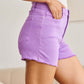 Woman wearing purple high waist raw hem denim shorts from RFM Jeans, showcasing a flattering tummy control fit.