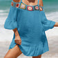 Woman wearing blue crochet cold shoulder three-quarter sleeve cover up with ruffled hem and colorful crochet details at the beach