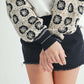 Close-up of a woman wearing a crochet contrast stitch V-neck top with intricate detailing and black shorts.