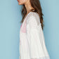 Woman wearing open front lace detail cardigan with 3/4 bell sleeves and frayed edges in a mix of jersey and lace, side view against blue background.