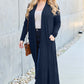 Woman wearing navy open front long sleeve cover up with pockets, paired with casual outfit and sunglasses, walking outdoors.