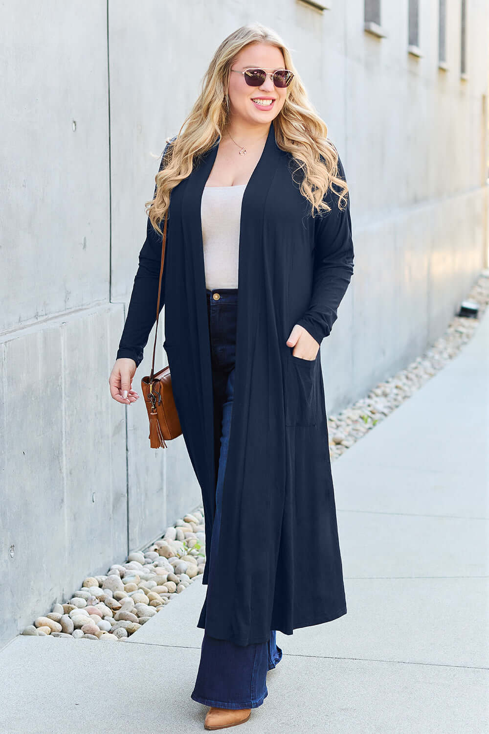 Woman wearing navy open front long sleeve cover up with pockets, paired with casual outfit and sunglasses, walking outdoors.